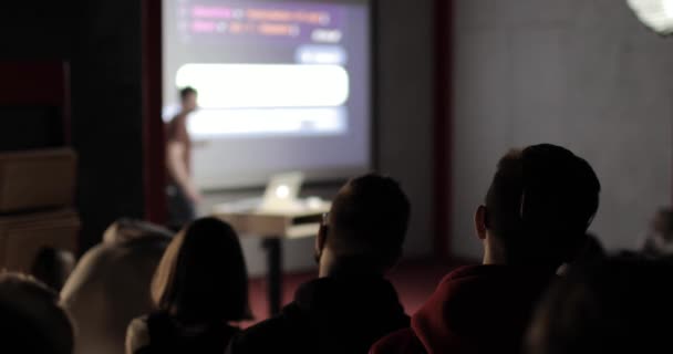 Grupa młodych ludzi słuchających wykładu wykładowcy-trenera za pomocą ekranu projekcyjnego i laptopa. — Wideo stockowe