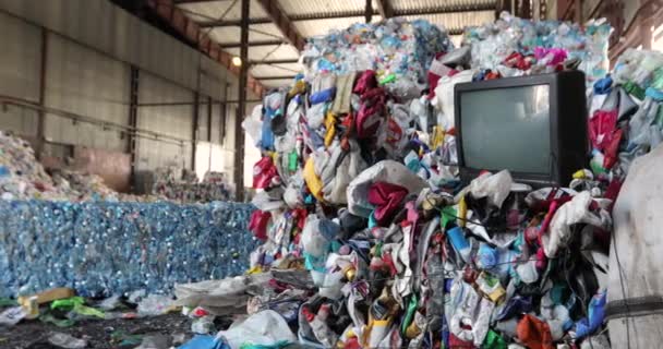 Un tas de déchets triés dans l'entrepôt. Briquettes en plastique, vêtements, TV. Gros plan. Recyclage et élimination. — Video