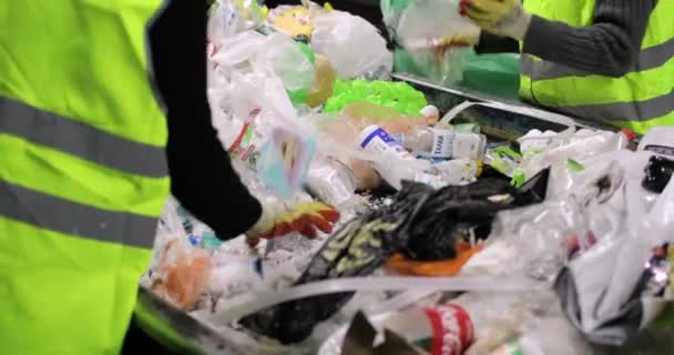 Pojemniki na śmieci są w środku. Stos różnych śmieci, plastiku, celofanu. Ludzie w rękawiczkach sortują śmieci ręcznie. Zbliżenie. — Wideo stockowe