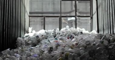 Depoda kapaklı ve etiketli bir sürü plastik şişe ve arka planda bir pencere var..