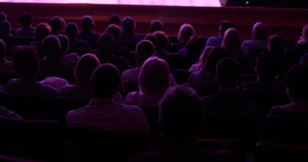 Spectators watch performance show or view in theater, back view. Staging in theatre. Many people in playhouse sitting in chairs and looking at scene. Full auditorium of people. — Stok Video