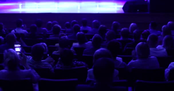 People at a conference or presentation, workshop, master class photograph. Back view. Staging in theatre. Many people in playhouse sitting in chairs and looking at scene. Full auditorium of people. — Stok video