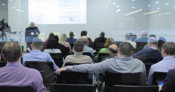 El público está escuchando al conferenciante en la sala de conferencias. Vista trasera. — Vídeos de Stock