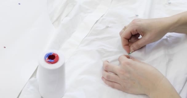 Las manos de los modistos cosen lentejuelas a la tela blanca. — Vídeo de stock