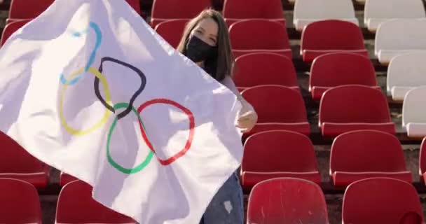 TOKYO, JAPONYAN - 21 Temmuz 2021 Olimpiyat oyunlarında olimpiyat bayrağı taşıyan koruyucu maskeli bir kadın boş bir podyumda ayakta duruyor. — Stok video