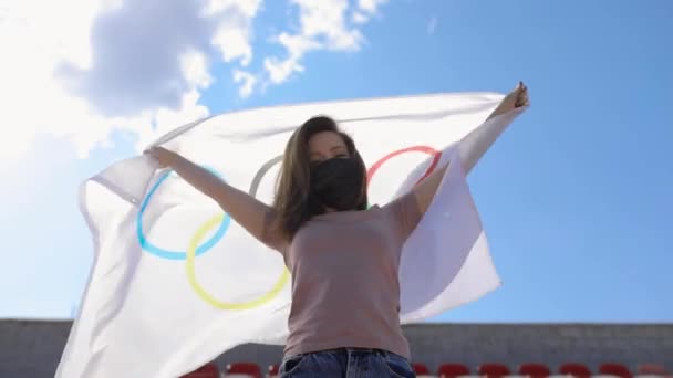 TOKYO, JAPAN - JULY 21, 2021: slow motion shot of a masked girl who is a fan of athletes at the Olympic Games, she is holding a flag with the symbols of the Olympics — Vídeo de stock