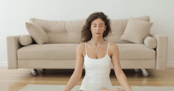 Ejercicios de yoga Una hermosa morena está haciendo yoga en la posición de loto en interiores y meditando. Vista frontal. — Vídeos de Stock