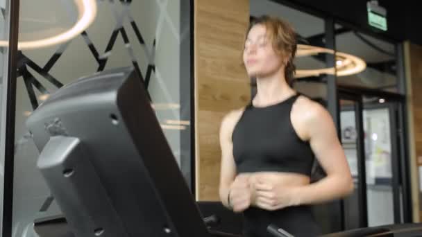 Young woman does cardio exercise on modern treadmill against glass door in sport club. — Stock Video