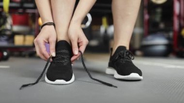 Spor salonunda ayakkabı bağcığı bağlayan genç bir kadının bacaklarına yakın çekim. Antrenmana hazırlanılıyor.