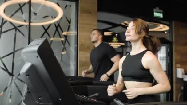 Sportowy młody mężczyzna i kobieta ćwiczą cardio na nowoczesnej bieżni w klubie sportowym. — Wideo stockowe