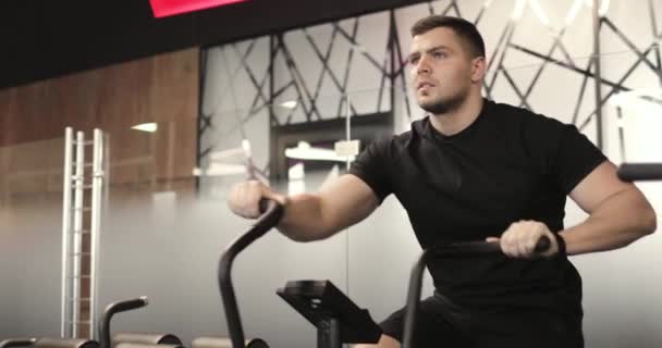 Portret van een sportieve jongeman die cardio doet op een stationaire fiets in de sportschool. — Stockvideo