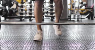 Beyaz spor ayakkabılı haltercinin spor salonunda halter kaldırışının kısmi görüntüsü. Ön görünüm.