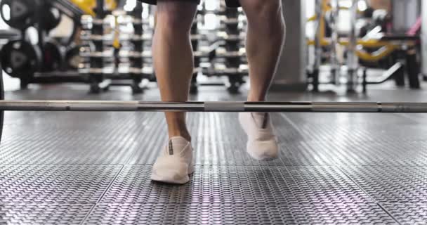 Vue partielle de l'haltérophile en baskets blanches soulevant l'haltère dans une salle de gym. Vue de face. — Video