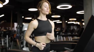 Genç atletik kadın spor kulübünde modern koşu bandında kardiyo egzersizi yapıyor..