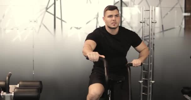 Кавказький спортивний молодий чоловік робить кардіоприймач на стаціонарному велосипеді в спортзалі. Передній вид. — стокове відео