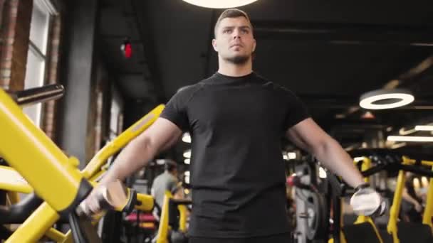 Retrato de hombre atlético con una camiseta negra haciendo ejercicios de bíceps en el gimnasio usando pesas. Vista frontal. — Vídeo de stock
