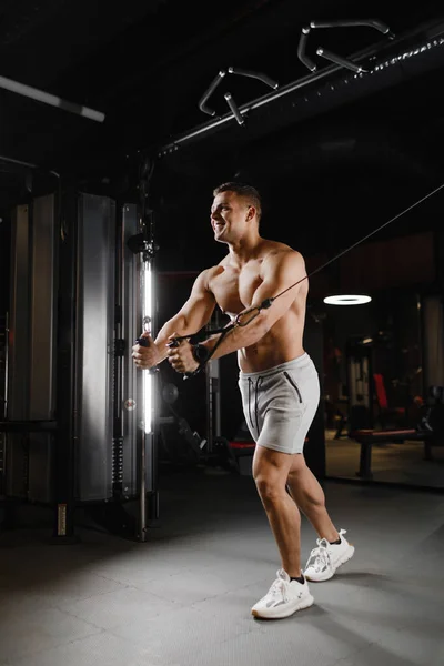 Type bodybuilder modèle avec un torse nu, trains dans la salle de gym. Les muscles sont tendus. Fond sombre. — Photo