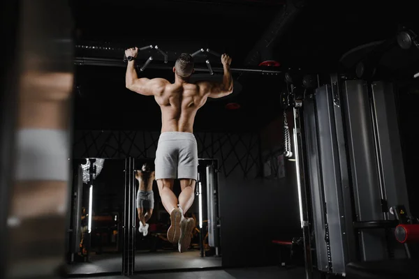 Homem de fitness bombeando músculo fazendo pull-ups exercícios no ginásio tronco nu. Bonitos homens atléticos fortes bombeando músculos traseiros treino fitness e musculação conceito fundo Fotos De Bancos De Imagens