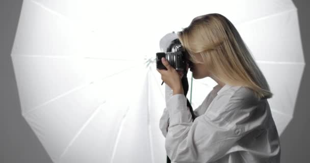 Hermosa joven fotógrafa en una camisa blanca con el pelo largo y rubio está trabajando en la toma de fotos. Vista lateral. — Vídeos de Stock