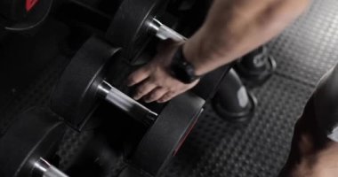 Akıllı saatli bir erkek, kürsüden bir dambıl alıp geri koyuyor. Spor salonunda. Yakın plan..