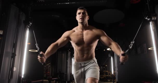 Atletische jongeman doet oefeningen voor biceps en buikspieren met behulp van een moderne expander. Vooraanzicht. — Stockvideo