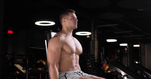 Sportlicher junger Mann, der im Fitnessstudio Kraftübungen mit Kurzhanteln im Sitzen macht. — Stockvideo