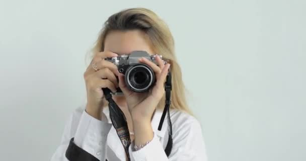 Portret van een jonge fotografe op een witte achtergrond in een wit shirt met een doorboorde neus en lang blond haar, die opnamen maakt. Lachen.. — Stockvideo