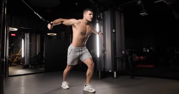 Snygg atletisk ung man gör övningar för biceps och abs med hjälp av en modern expander. Full längd. — Stockvideo