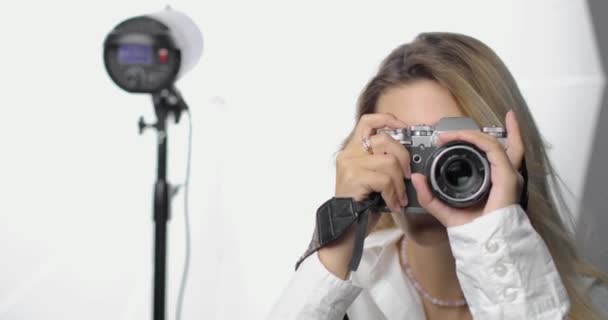 Retrato de uma jovem fotógrafa elegante em uma camisa branca com um nariz perfurado e longos cabelos loiros, fazendo tiros. Sorrindo.. — Vídeo de Stock