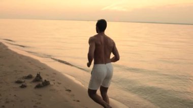 Güzel, yumuşak bir gün doğumu ya da gün batımı ve sis. Beyaz şortlu, kumsalda koşan atletik bir genç. Ağır çekim. Arka plan.