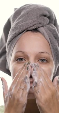 Cildini önemseyen, yüzünü doğal köpük temizleyicisiyle masaj hareketleriyle temizleyen güzel bir kadının yüzü. Dikey video.