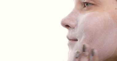 Cildini önemseyen beyaz bir kadının yüzüne yakından bakın. O, köpük jel kullanarak yüzünü masaj hareketleriyle temizler. Yan görünüm.