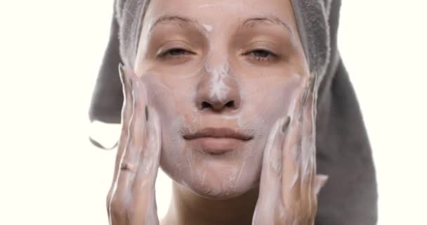 Portret młodej pięknej kobiety z ręcznikiem na głowie myjącej twarz środkiem czyszczącym. Dziewczyna oczyszcza skórę twarzy, wykonuje ruchy masażu. Widok boczny. — Wideo stockowe
