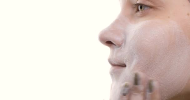 Close-up van het gezicht van een jonge blanke vrouw die voor haar huid zorgt. Ze reinigt het gezicht met massagebewegingen met haar handen met een schuimgel. Zijaanzicht. — Stockvideo
