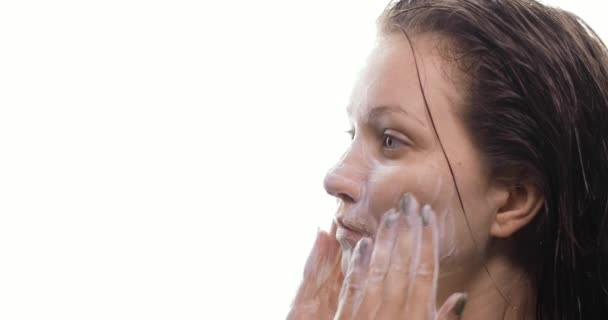 Крупним планом молода жінка з мокрим волоссям очищає обличчя органічним пінистим засобом для чищення після прийняття душу. Дівчина очищає шкіру обличчя, робить масажні рухи. Вид збоку . — стокове відео