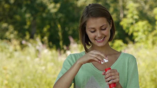 Young beautiful woman blows soap bubbles in park — Stock Video