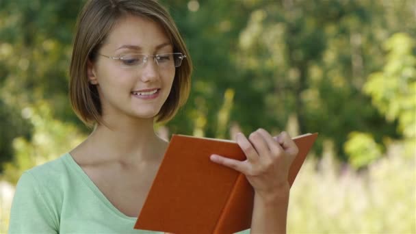 Молода жінка читає книгу з помаранчевою обкладинкою — стокове відео