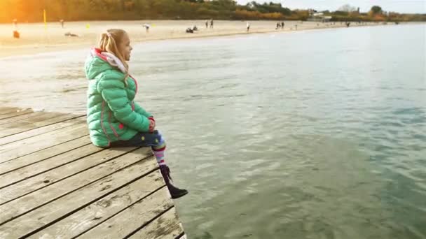 Pequeña chica hermosa se sienta en el muelle de madera — Vídeo de stock