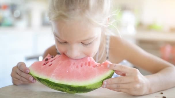 Schöne blonde kleine Mädchen essen Wassermelone auf dem Hintergrund der hellen Küche. — Stockvideo