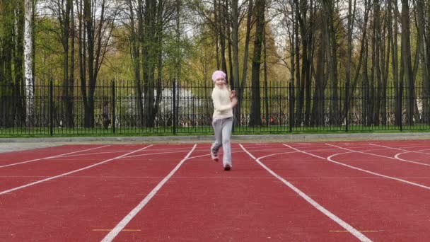 Pequena menina bonita correndo em um caminho em um estádio ao ar livre . — Vídeo de Stock