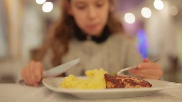 Маленькая красивая девочка ест пюре и свиные отбивные в ресторане . — стоковое видео