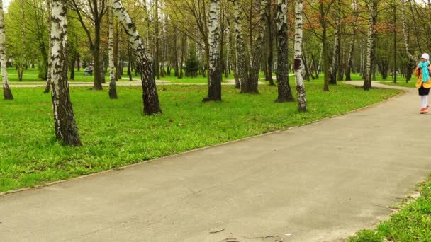 Malá krásná dívka ve žlutém kabátě a batohu chodí do školy na podzim. — Stock video