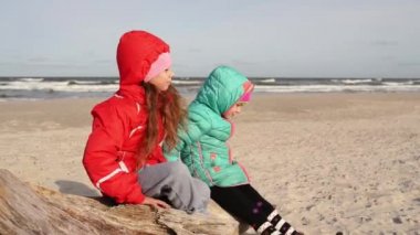 Hood ile ceket küçük güzel kızlar dalgaların karaya attığı odun Baltık Denizi kıyısında oturur ve mesafe içine bakıyor.