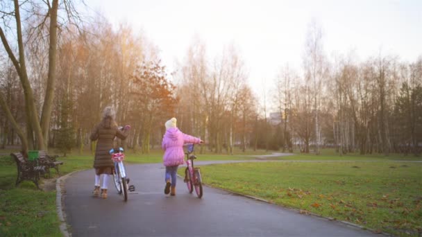 Dos niñas hermosas montando bicicletas en el parque de otoño de la ciudad . — Vídeo de stock