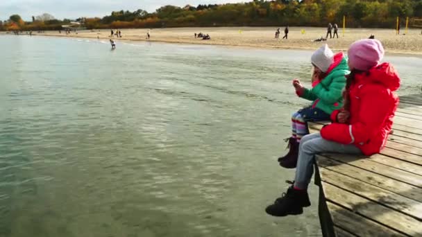 Två små vackra flickor sitta på en träbrygga i Sopot, Polen. — Stockvideo