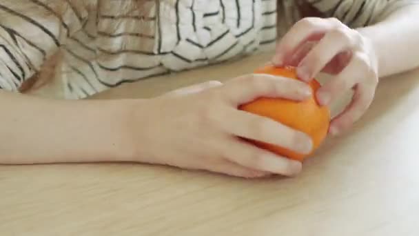 Little beautiful girl peels ripe orange at the table in the kitchen. — Stock Video