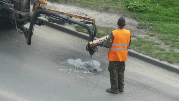 4k Trabajador de la construcción reparando agujeros en la carretera con grava y betún con la ayuda de equipos especiales . — Vídeo de stock