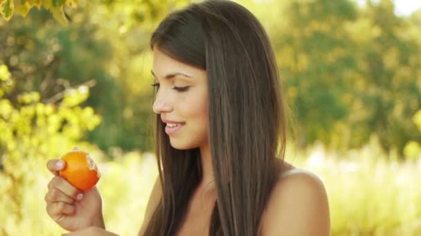 Jovem mulher bonita sorridente limpa laranja, contra o fundo do parque de outono . — Vídeo de Stock