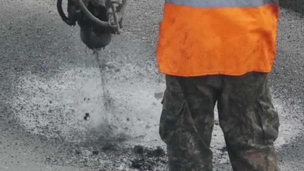 特別な装置の助けを借りて、アスファルトや砂利道路上の穴を修復する建設労働者. — ストック動画