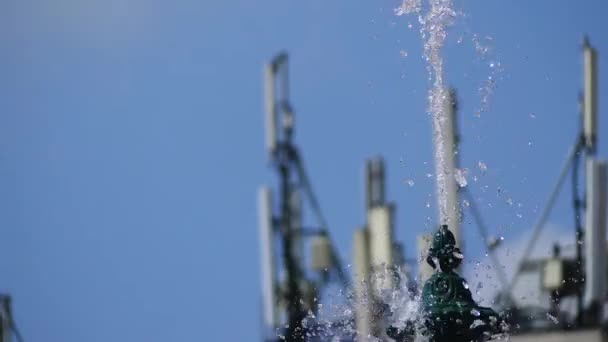 Ein kleiner Springbrunnen vor blauem Himmel mit Wolken und Telekommunikationsantennen. — Stockvideo